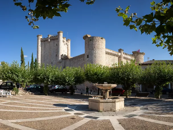 Castillo medieval junto a plaza arbolada.