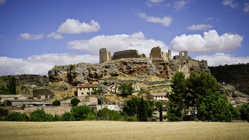 Ruinas de fortaleza medieval sobre colina rocosa junto a un núcleo urbano