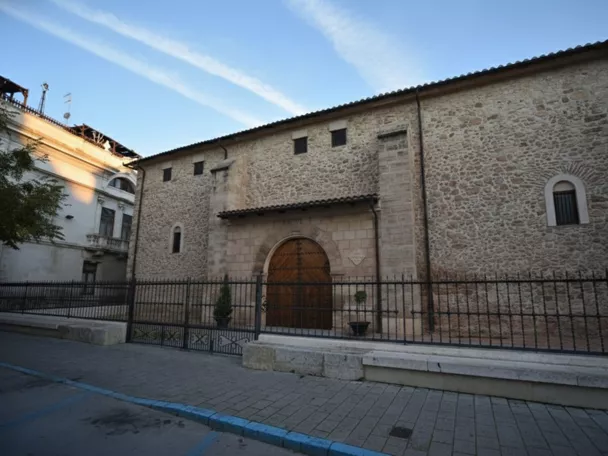Fachada de edificio histórico de piedra con arco de entrada y reja metálica al frente.