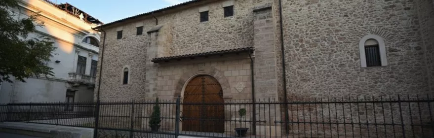 Fachada de edificio histórico de piedra con arco de entrada y reja metálica al frente.