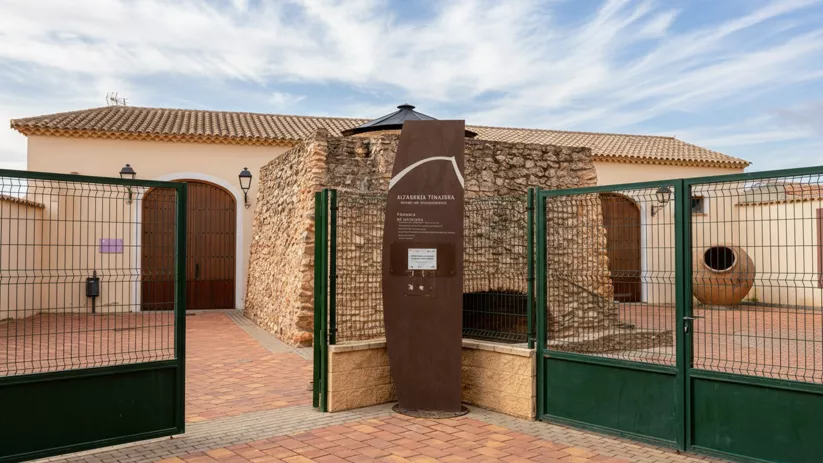 Entrada vallada con panel informativo, puertas de madera y patio empedrado.