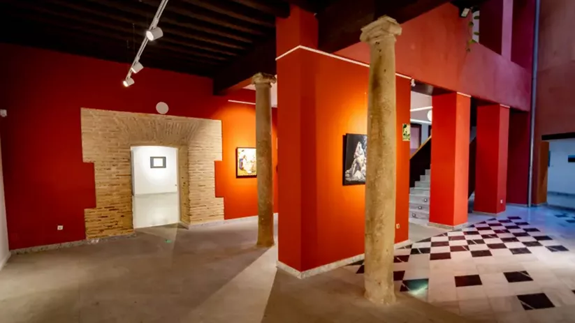 Espacio interior con paredes rojas, columnas de piedra y suelo ajedrezado.