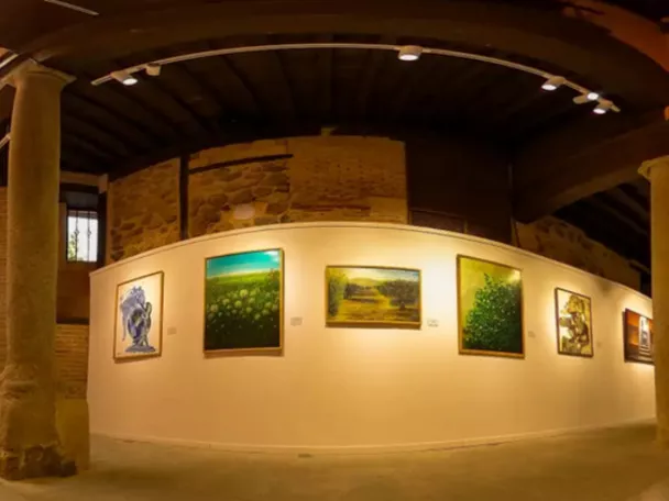 Sala de exposiciones con paredes curvas, columnas de piedra y cuadros colgados.