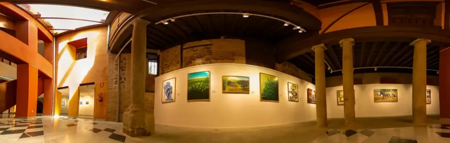 Sala de exposiciones con paredes curvas, columnas de piedra y cuadros colgados.
