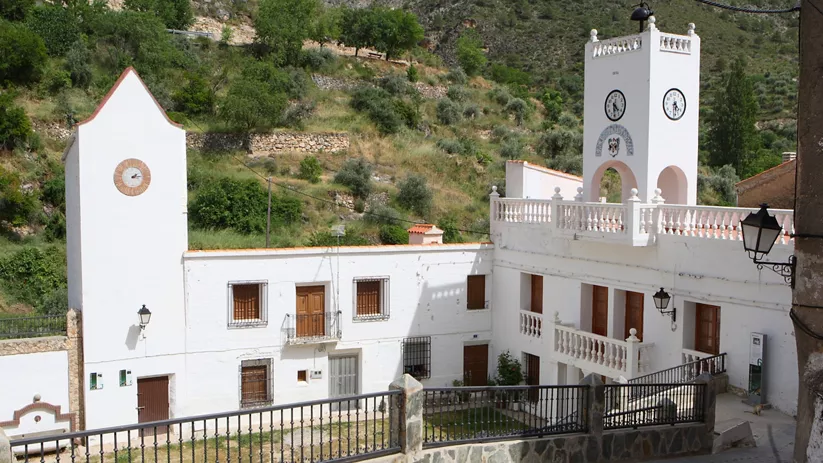 Conjunto de edificios blancos con torre de reloj en un entorno rural.