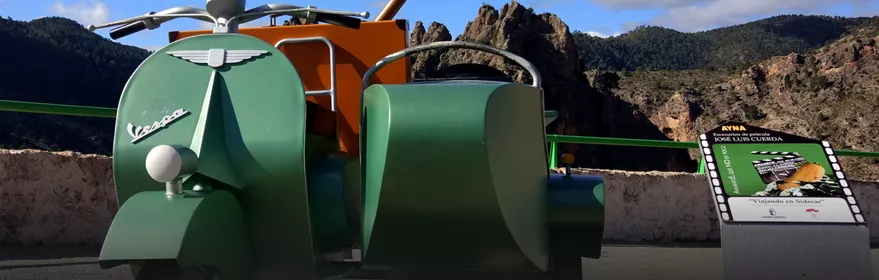 Escultura de motocicleta con sidecar frente a un paisaje montañoso.