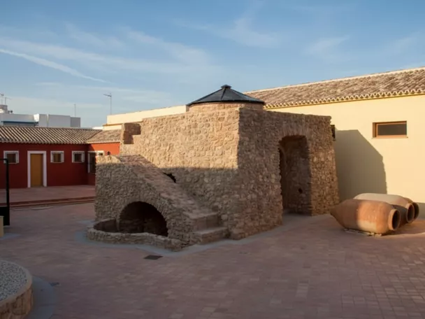 Vista lateral de un horno de piedra en una plaza, con tinajas en el suelo.
