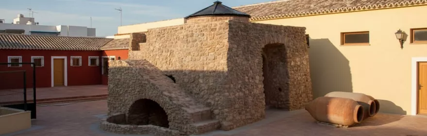 Vista lateral de un horno de piedra en una plaza, con tinajas en el suelo.