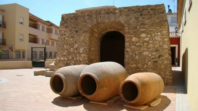 Primer plano de tres tinajas de barro frente a un arco de entrada de piedra.