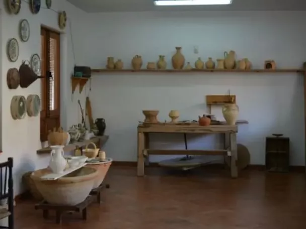 Sala con mesa de trabajo y piezas de alfarería expuestas en estantes.