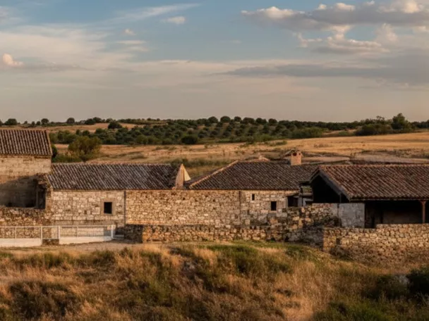 Panorámica del conjunto de piedra con tejados bajos y campos abiertos alrededor.