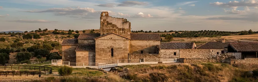 Panorámica del conjunto de piedra con tejados bajos y campos abiertos alrededor.