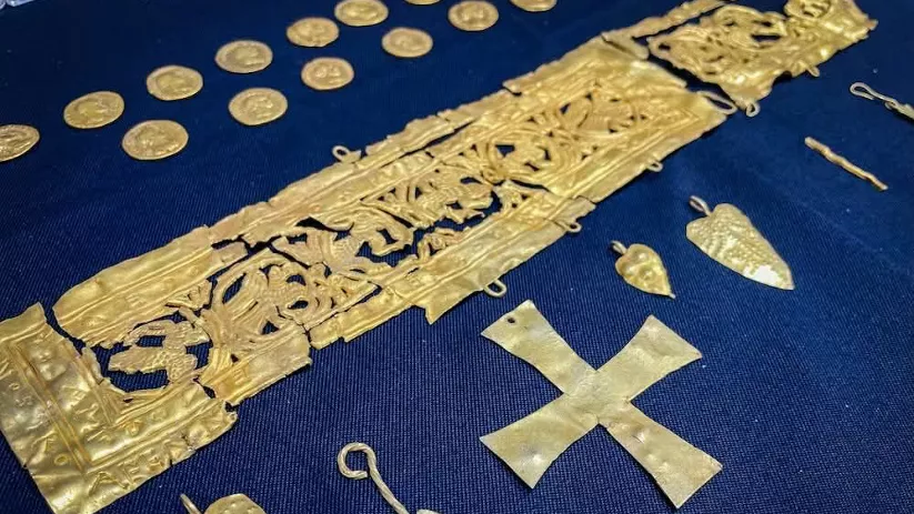 Objetos y adornos de oro antiguos colocados sobre tela azul.