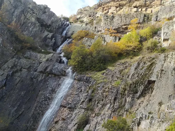 Cascada escalonada entre paredes rocosas y vegetación otoñal.