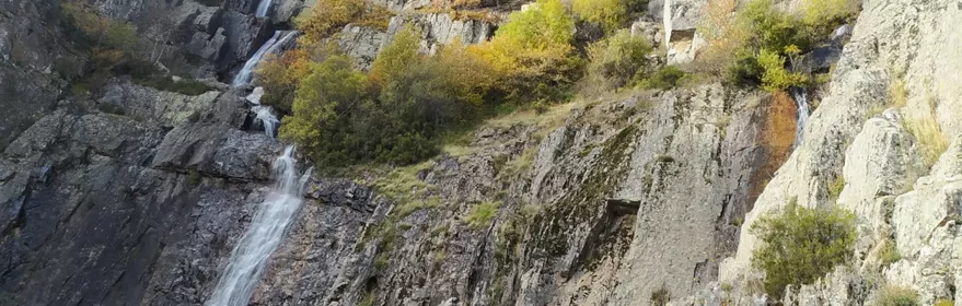 Cascada escalonada entre paredes rocosas y vegetación otoñal.