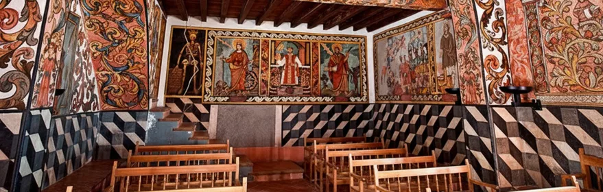 Sala con bancos y paredes decoradas con frescos religiosos.