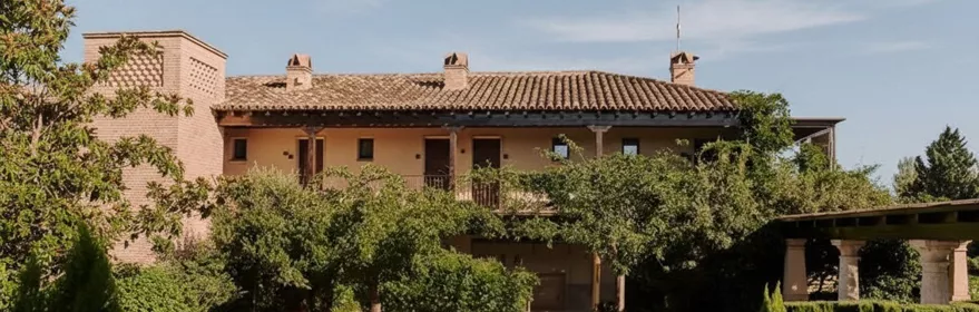 Fachada de edificio rústico rodeado de jardines y setos.