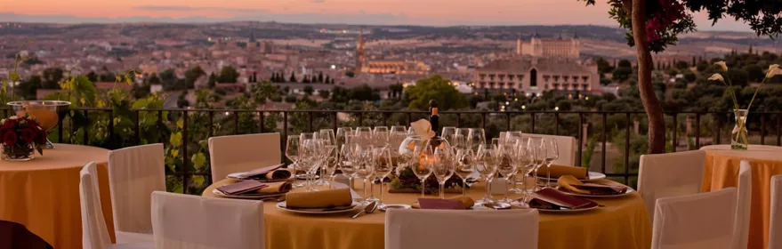 Mesa montada en terraza con copas y vistas de la ciudad al atardecer.