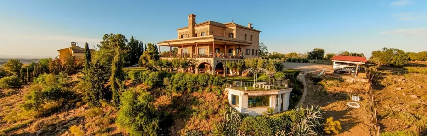 Casa en ladera con porche, jardines y camino de acceso.