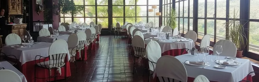 Salón acristalado con mesas vestidas y vistas al paisaje.