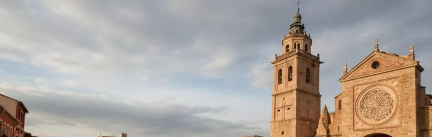 Plaza amplia con iglesia de piedra y torre junto a edificios tradicionales.