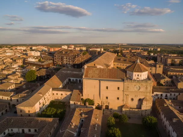Vista aérea de un casco urbano con un gran edificio religioso de piedra al atardecer.