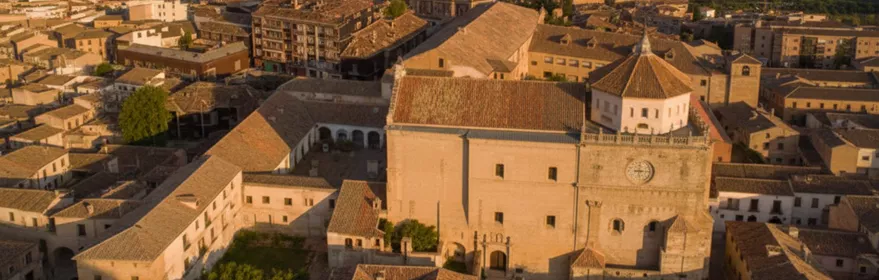 Vista aérea de un casco urbano con un gran edificio religioso de piedra al atardecer.