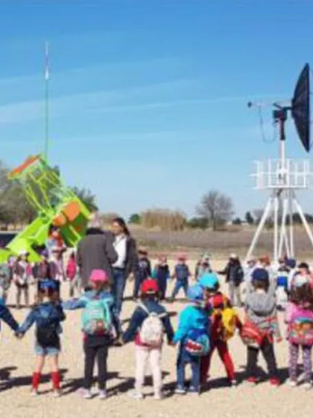 Grupo de niños en visita escolar al aire libre junto a instrumentos científicos.