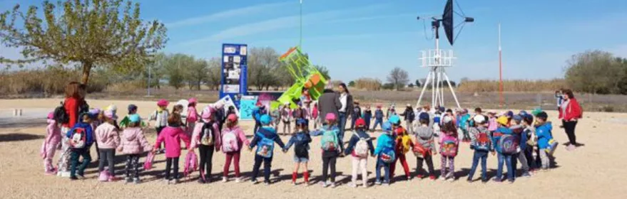 Grupo de niños en visita escolar al aire libre junto a instrumentos científicos.
