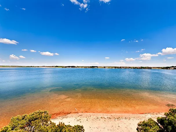 Orilla de laguna con aguas tranquilas y cielo despejado.