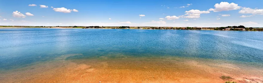 Orilla de laguna con aguas tranquilas y cielo despejado.