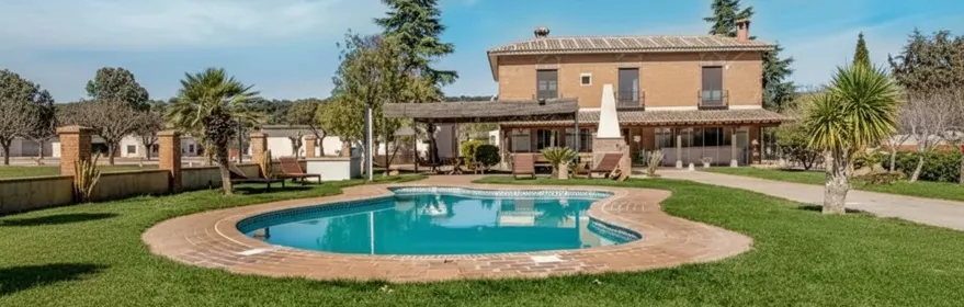 Casa rural con piscina rodeada de césped y palmeras