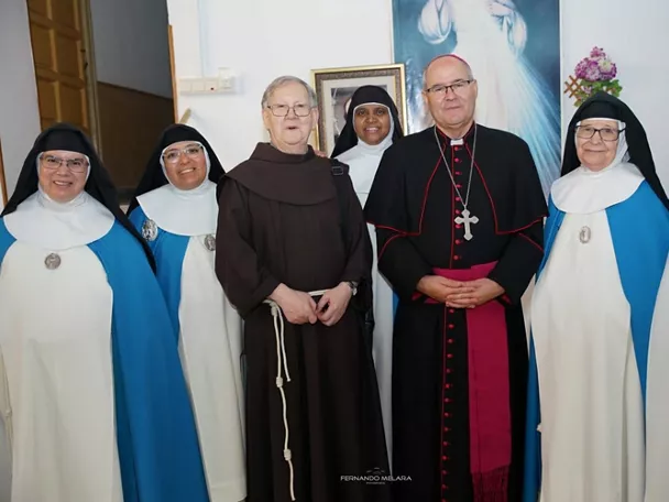 Grupo de religiosas y clérigos posando en una sala junto a un cuadro.