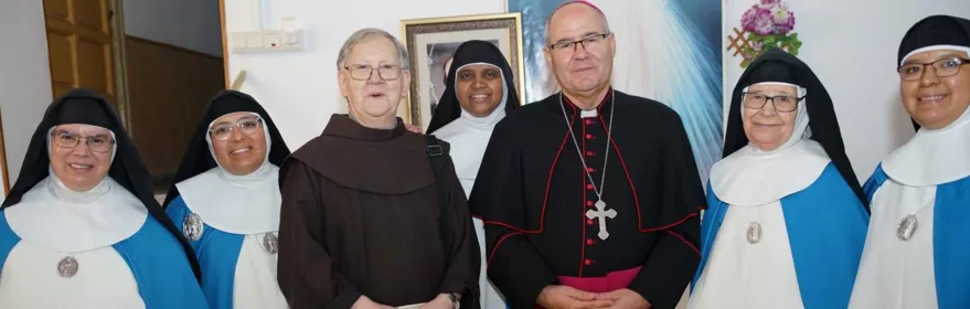 Grupo de religiosas y clérigos posando en una sala junto a un cuadro.