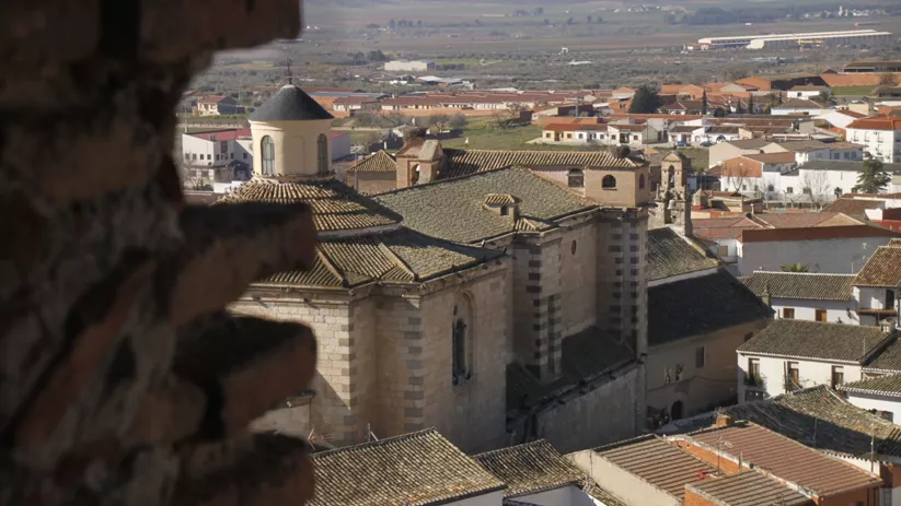 Vista elevada de una iglesia de piedra entre los tejados del casco urbano.