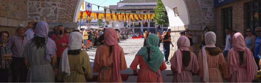 Grupo de personas con vestimenta medieval observando un desfile desde un arco de piedra.