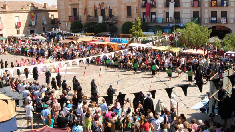 Vista aérea de una plaza abarrotada durante una recreación histórica con estandartes y público.