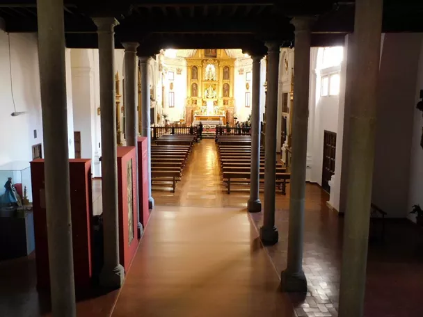 Interior de iglesia con columnas, bancos de madera y altar dorado al fondo.