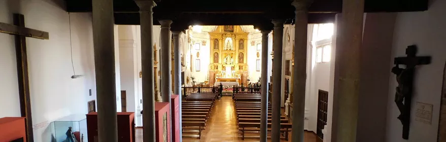 Interior de iglesia con columnas, bancos de madera y altar dorado al fondo.