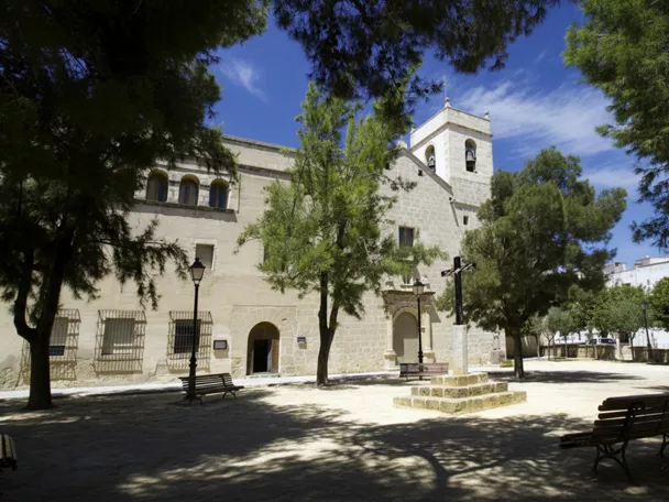 Fachada de iglesia con torre campanario y plaza arbolada.