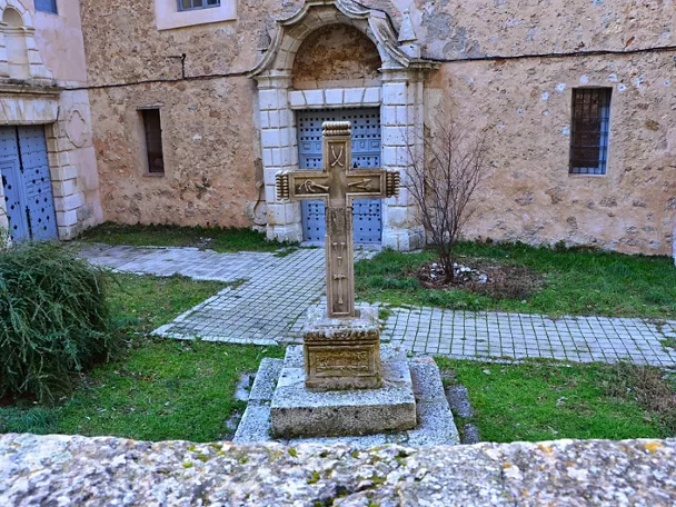 Cruz de piedra en patio con fachada histórica