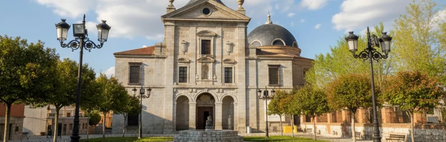 Fachada principal de iglesia con cúpula, torre y plaza ajardinada.