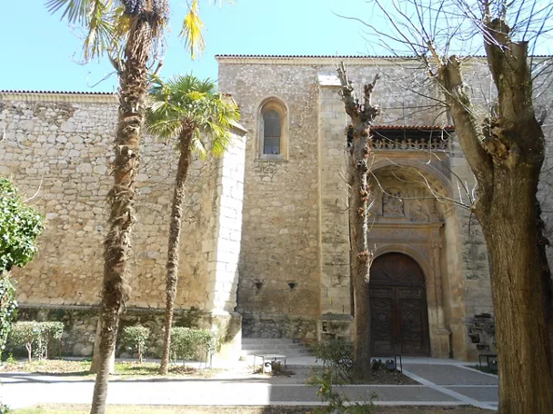 Fachada histórica de piedra entre jardines urbanos.