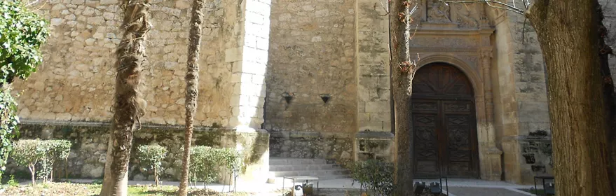 Fachada histórica de piedra entre jardines urbanos.