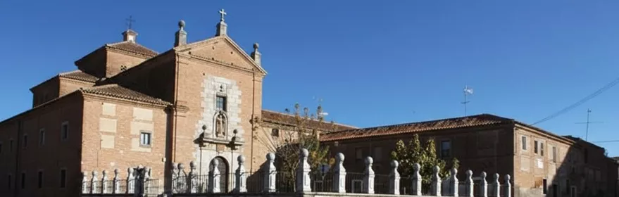 Fachada de iglesia de ladrillo con cruz superior y verja de piedra junto a la calle.