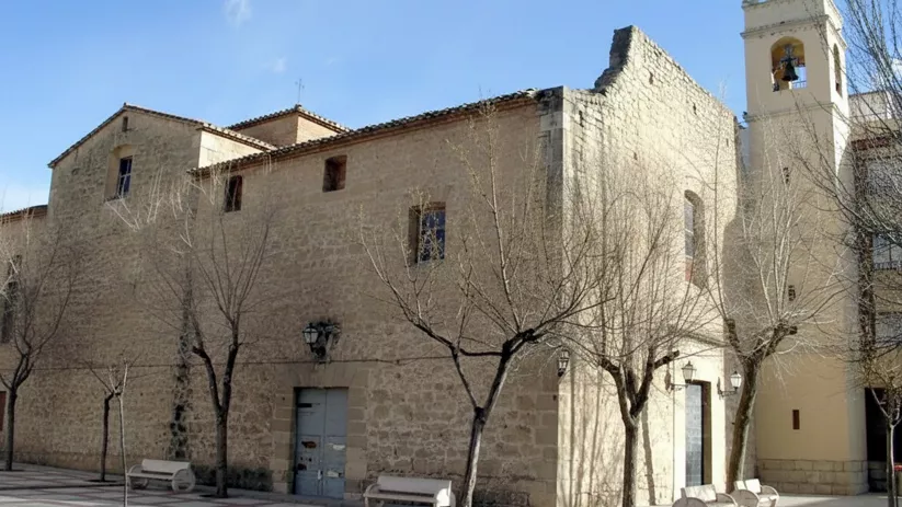 Iglesia de piedra clara con campanario alto en plaza pavimentada.
