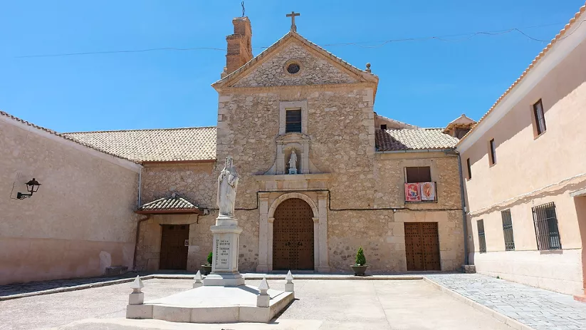Fachada de iglesia de piedra con estatua y atrio central                  