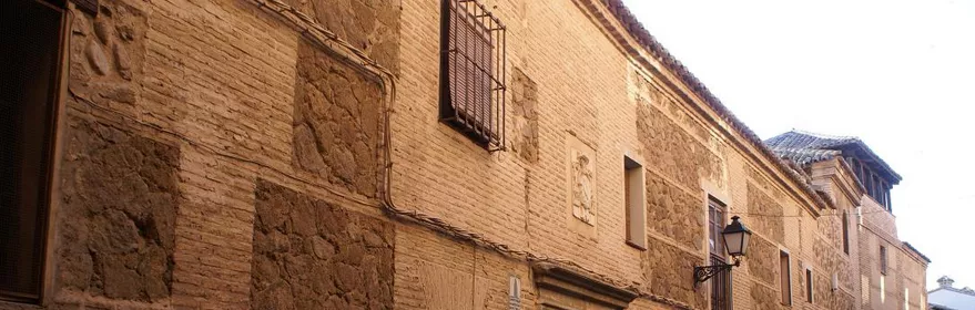 Fachada de edificio histórico con muros de piedra y ladrillo en una calle estrecha.