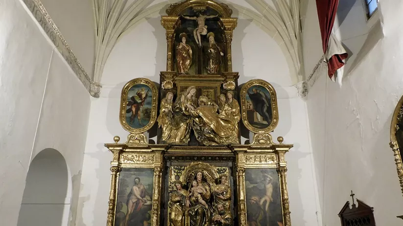 Retablo dorado con relieves y figuras religiosas en una capilla de nave alta.