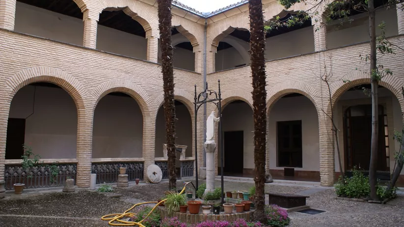 Claustro con arcos de ladrillo, patio central y plantas ornamentales.